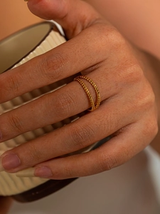 Detail of a golden double-row milgrain ring worn while holding a beige ceramic cup