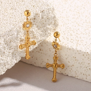 Détail macro de boucles d'oreilles en acier doré 18K avec pendentif croix et cristal solaire
