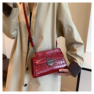 Detail of red crocodile pattern crossbody bag with unique metal buckle on trench coat
