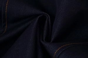 Détail macro du tissu denim bleu foncé avec doubles surpiqûres orange et texture en sergé