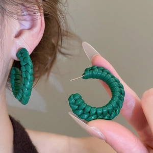 Close-up of green hand-woven leather C-shaped earrings with silver needles for women