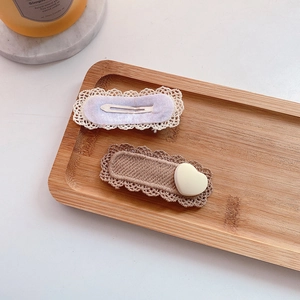 Detail of cute knitted hair clips with white lace edges and a cream heart on wood tray