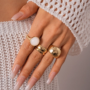 Detail shot of model wearing gold wide band rings and white oval stone ring set