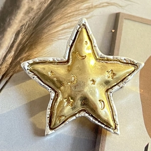 Gros plan d'une broche étoile dorée et argentée mate avec motif de lune en relief