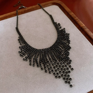 Detailed view of gunmetal tassel necklace with multi-row rhinestones on a wooden tray