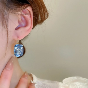 Close-up of light blue cushion-cut gemstone drop earring on model with golden hook