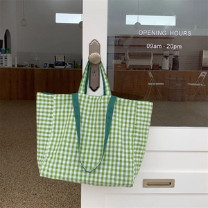 Green and white checkered canvas tote bag hanging on a vintage door handle in a cafe
