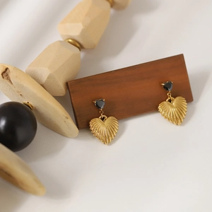 Golden heart earrings with black stone studs on wooden stand, minimalist style