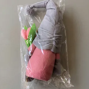 Gnome plush toy with pink tulip in plastic packaging against a brown cardboard box