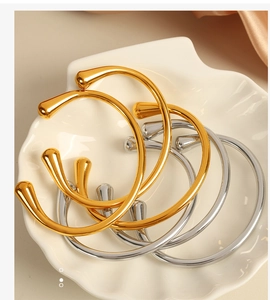 Dettaglio di bracciali aperti lucidi oro e argento in un piatto di ceramica a forma di conchiglia