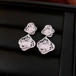 Macro shot of silver-toned hollow flower petal earrings on a black leather jewelry box