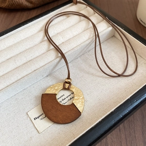 Detail of round wood and hammered gold pendant with leather cord in a jewelry box