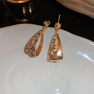 Detailansicht goldener tropfenförmiger Ohrringe mit Kristallen auf weißer Keramikplatte