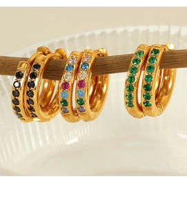 Détails macro des boucles d'oreilles huggies dorées avec zircons colorés, noirs et verts