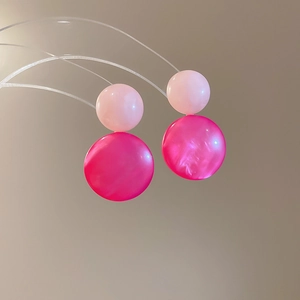Close-up of resin round drop earrings with pearlescent finish and pink gradient tones