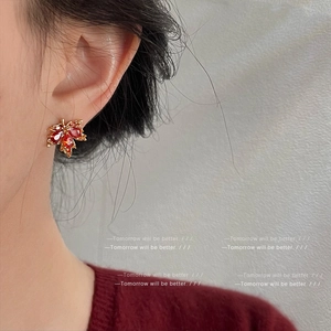 Boucles d'oreilles feuille d'érable en or et zircon rouge portées par un mannequin élégant