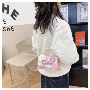 Pink tweed children's crossbody bag with pearl handle and bow detail on a model