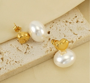 Detail of heart-shaped gold pearl earrings on stone with elegant fabric texture