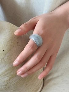 Detail of gray marbled resin ring worn on finger against minimalist ceramic background