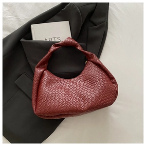 Flat lay of a burgundy woven crescent handbag with a knotted handle on a white fabric