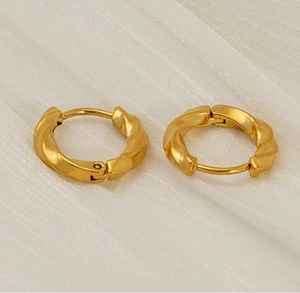 Detail of gold-plated twisted hoop earrings with a textured spiral design on beige fabric