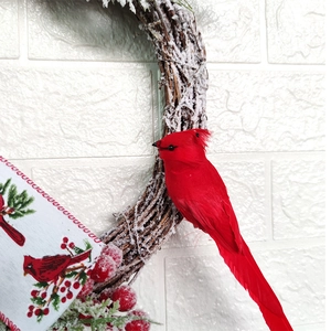 Detail of red cardinal bird on snow-flocked wreath with berries and ribbons