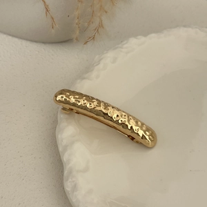 Close-up of golden hammered metal hair clip with textured surface on ceramic plate
