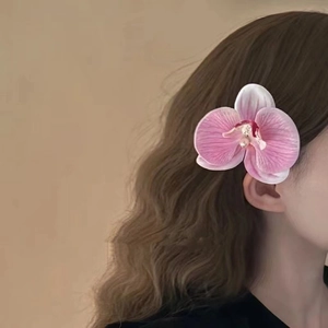 Detail of pink orchid hair clip worn on model's hair for a natural floral styling look