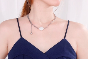Detail of silver asymmetric chain necklace with round white shell pendant on model