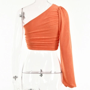 Gros plan détaillé du haut court orange à une épaule avec une texture plissée chic