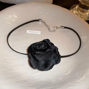 Elegant black satin camellia choker necklace with silver clasp in a minimalist white tray