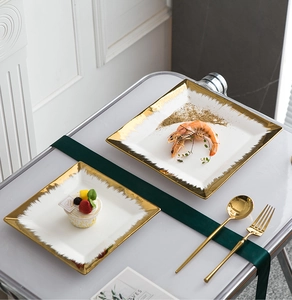 Close-up of square white ceramic plates with irregular gold edges on marble table