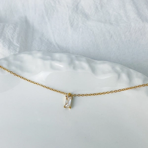 Detail of a minimalist gold necklace with a clear rectangular zircon pendant on a tray