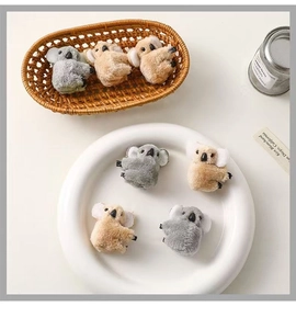 Close-up of cute plush koala hair clips in grey and tan colors in a woven basket
