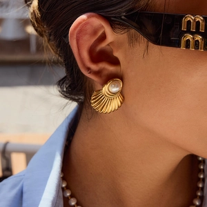 Close-up of a gold shell-shaped earring with pearl inlay worn by a female model