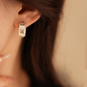 Detail of C-shaped gold plated white enamel earring with square gemstone on model ear