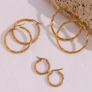 Detailed view of three pairs of twisted gold hoop earrings on a textured stone surface