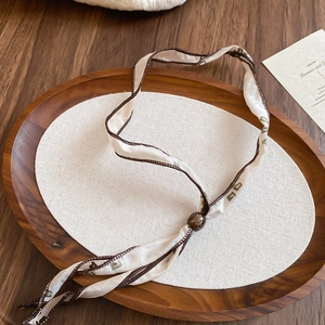Macro shot of ethnic style silk ribbon necklace with tiger eye stone bead on wooden tray
