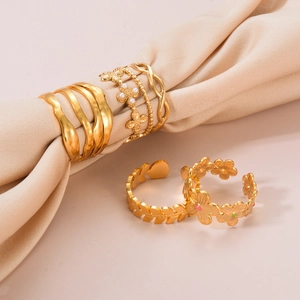 Gold stainless steel flower and leaf rings with pearls on a soft beige fabric