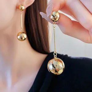 Minimalist double metal sphere drop earrings in gold finish worn by a model