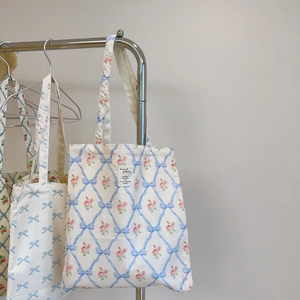 Detail of floral tote bags with blue ribbon patterns hanging on a metal rack