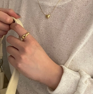 Close-up of a gold knotted silver ring and heart pendant necklace worn by a model