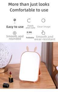 Detail view of foldable coral rabbit ear makeup mirror with stand on wooden desk