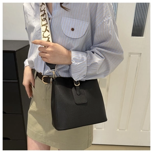 Detail of black leather bucket bag with a patterned wide strap worn by a model