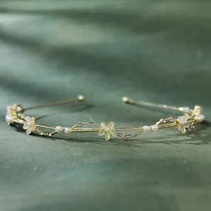Detail of gold leaf headband with cat-eye flowers and pearls on green velvet background