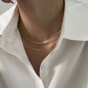 Double-layered gold snake bone necklace and delicate chain on a model wearing white shirt