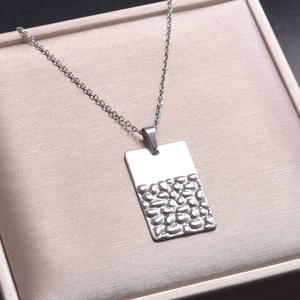 Détail macro d'un pendentif rectangulaire argenté avec une finition martelée et polie