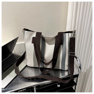 Striped canvas tote bag with brown straps placed on metal shelf for office use