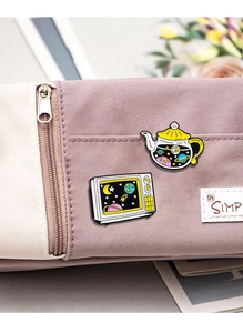 Detail of star-themed teapot and vintage TV enamel pins on a purple canvas bag
