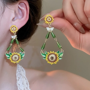 Macro detail of sunflower and bee earrings featuring green beads and yellow enamel finish